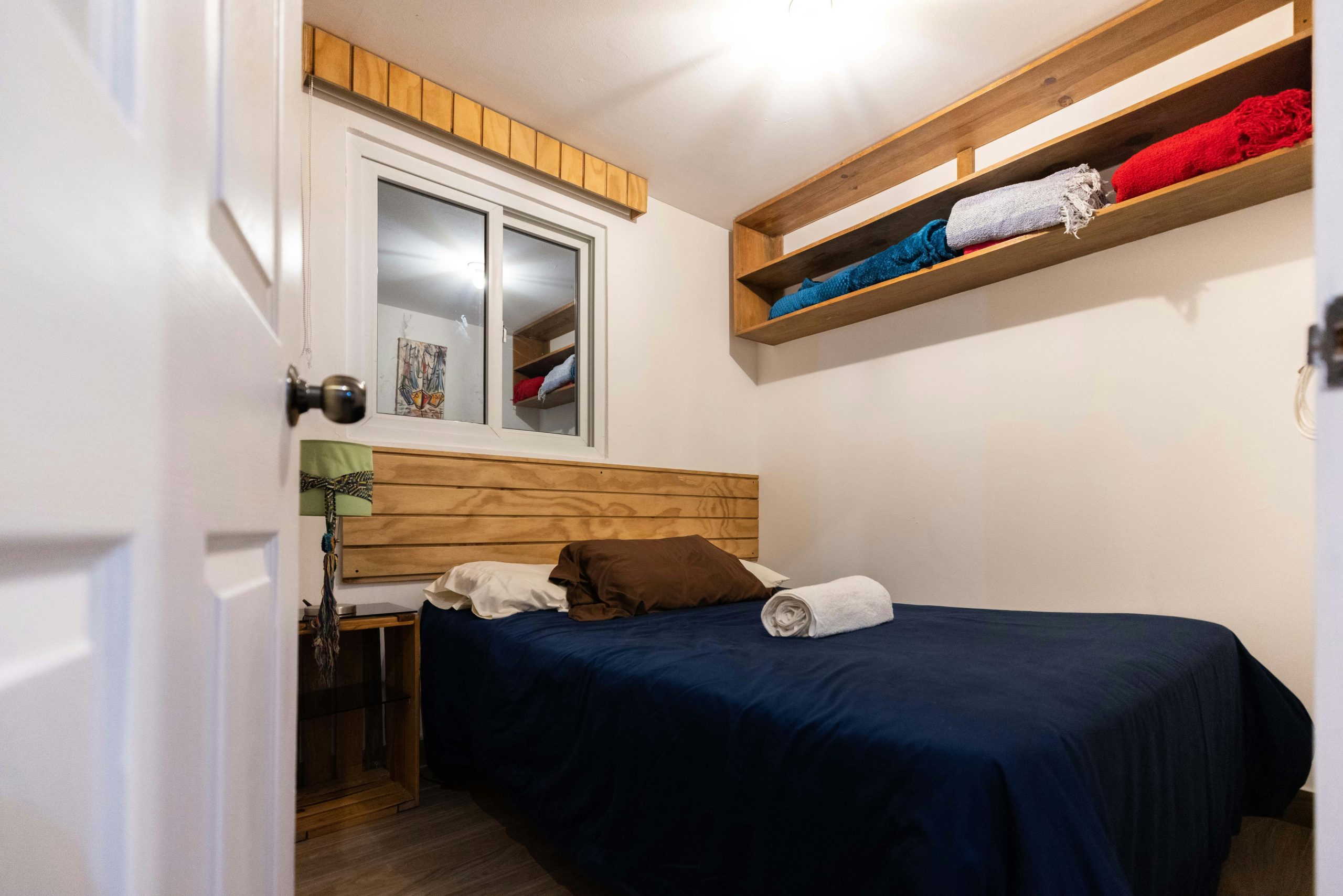 Small bedroom with wooden headboard, floating shelves, and window