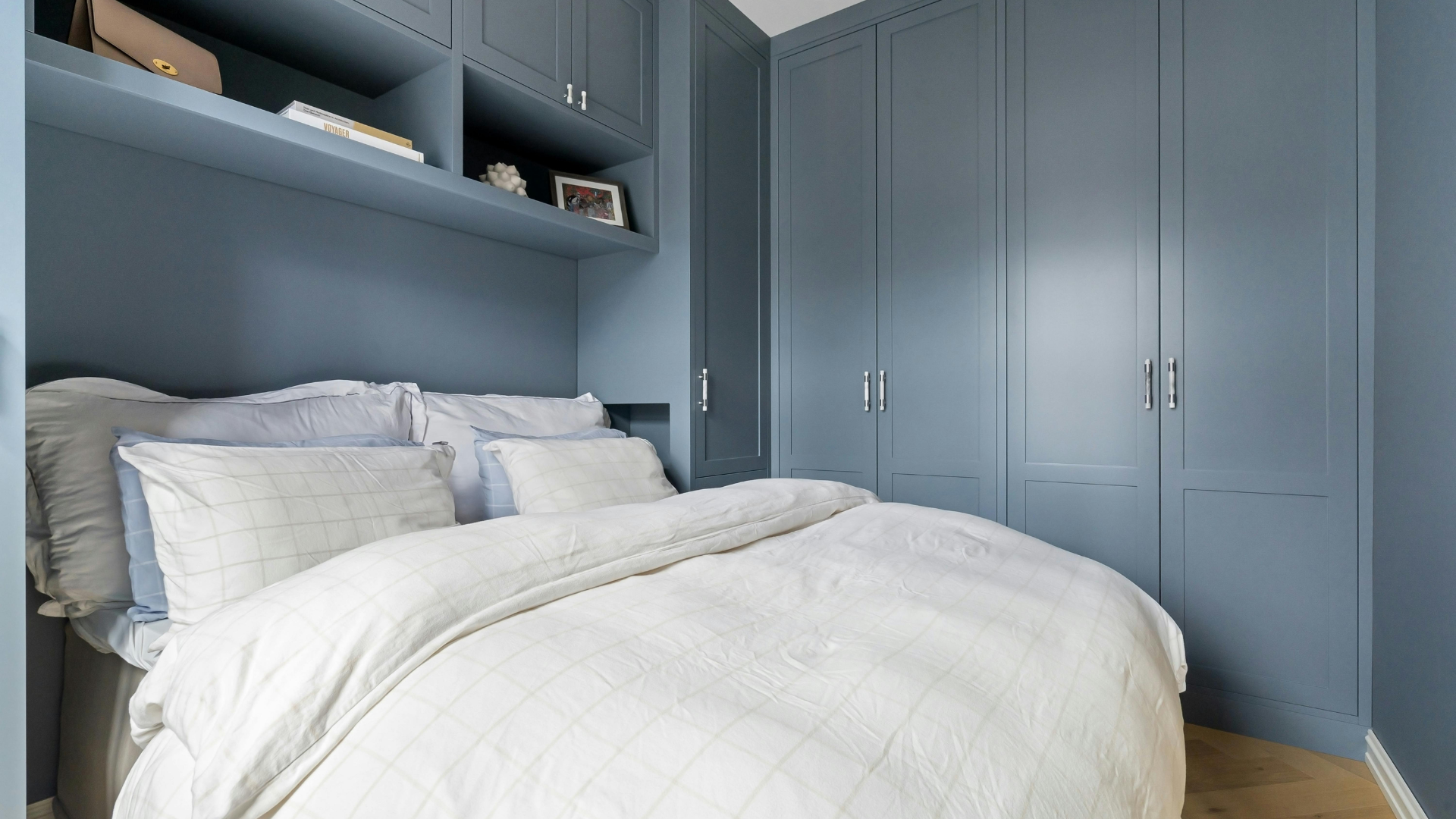 Fitted blue cabinetry and shelving surrounding a bed